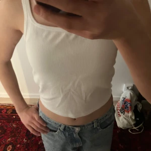 Vit ribbad linnetopp från Uniqlo - Säljer en vit ribbad linnetopp från Uniqlo Airism med inbyggda kupor. Toppen är croppad och har smala axelband. Perfekt för varma dagar och enkel att styla med jeans eller kjol. Materialet är mjukt och stretchigt för extra komfort. Passar bra för träning!🥰