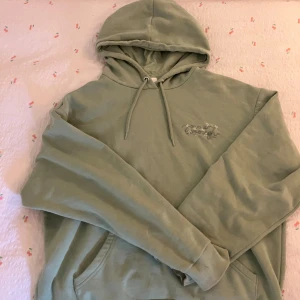 Grön hoodie från Monki med broderi - Säljer en ljusgrön hoodie från Monki i storlek XS. Tröjan har huva med snörning, magficka och broderad text 'You are enough' med små blommor på bröstet. Perfekt för chill dagar och enkel att matcha med jeans eller leggings.