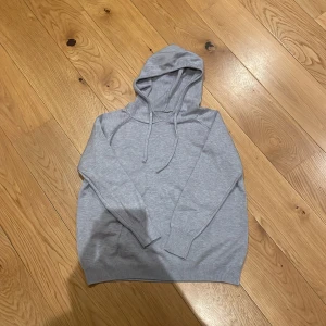 Ljusgrå hoodie med huva - Enkel och stilren ljusgrå hoodie med huva och snörning. Tröjan har långa ärmar och ribbade muddar vid ärmslut och nederkant. Perfekt för en avslappnad look och passar året runt.