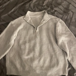 Ljusgrå stickad half zip-tröja - Säljer en ljusgrå stickad tröja med half zip och hög krage. Tröjan har en grovstickad struktur och långa ärmar, perfekt för lager på lager. Enkel och stilren design som funkar till allt.