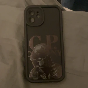 iPhone 12 Skal med CP Company Motiv - Snyggt och robust skal till iPhone 12 med unikt CP Company-motiv. Skalets skick är mycket bra, helt nytt! Perfekt passform för kameran och knappar. Skyddar din mobil mot stötar och repor samtidigt som det ger en personlig stil. Pris kan diskuteras!