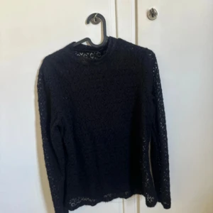 Svart spetsblus med lång ärm - Säljer en svart blus med lång ärm i genombruten spets. Toppen har en rund hals och ett snyggt mönster i spetsen som gör den extra cool. Perfekt att styla med jeans eller kjol för en  trendig look.