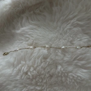 Guldarmband med pärlor - Snyggt och tunt armband i guld med små vita pärlor jämnt utspridda längs kedjan. Perfekt för dig som gillar stilrena och eleganta smycken med en touch av lyx. Lätt att matcha med andra accessoarer och passar till alla tillfällen.
