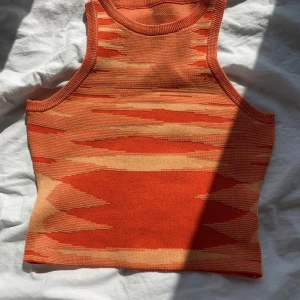 Stickad orange topp - Säljer ett stickat linne i orange och beige med ett coolt abstrakt mönster. Perfekt för dig som gillar färg och unika detaljer i din garderob.