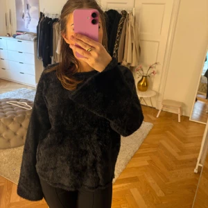 Svart fluffig tröja - Mysig svart tröja i supermjuk fuskpäls. Långärmad modell med rund hals och relaxed fit. Perfekt för kalla dagar när du vill vara både varm och mysig