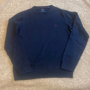 Mörkblå bomullströja från Gant - Säljer en stilren mörkblå tröja från Gant i premium bomull. Tröjan har rund hals, ribbade muddar och diskret broderad Gant-logga på bröstet i rött. Perfekt för dig som gillar klassisk och clean stil. Storlek S. Inga defekter! Har du frågor? Skriv! Så svarar jag så snart som möjligt! MVH SWISSWEAR🇨🇭🍾🏔️