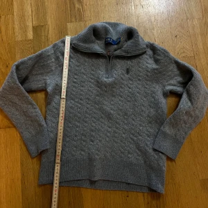 Grå stickad tröja Polo Ralph Lauren - 🛑OBS! Kolla beskrivningen snälla!!  Storlek: M (men har krympt)! Säljer en klassisk grå kabelstickad tröja från Polo Ralph Lauren med halvlång dragkedja i kragen. Tröjan är ursprungligen i storlek M och köptes för cirka ett år sedan på Magasin i Danmark. Den har handtvättats enligt anvisningarna, men råkade därefter tvättas i 40 grader tillsammans med andra kläder, vilket gjort att den krympt och nu motsvarar ungefär en XS i passform (eller barnstorlek 140 cl,10år). Axel bredd = 40cm, längd 48cm