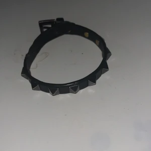 Valentino Armband - Säljer ett svart armband från Valentino. Smycket är gjort i skinn och har ett klassiskt spänne i metall. Perfekt accessoar för att ge din outfit en extra touch. Extra nitar ingår samt originalförpackningen. Lite slitet som man ser på bilderna men annars inga problem.