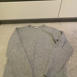 Grå stickad tröja från Kappahl - Mysig grå stickad tröja från Kappahl i storlek 170. Tröjan har rund halsringning och långa ärmar med ribbade muddar. Perfekt för dig som gillar enkel och stilren look. Materialet är mjukt och passar bra när det är lite kyligt ute. Lite nopprig, visas på sista bilden därför jag säger för 30kr