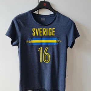 Blå Sverige t-shirt med nummer 16 från Stadium strl S - Mörkblå t-shirt från Stadium med tryck i gult och blått: 'Sverige' och siffran 16 på framsidan från Stadium. Gjord i 100% bomull och har en klassisk rund hals och korta ärmar. Storlek S. Kan hämtas i Vallentuna.