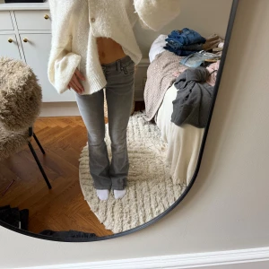 Grå bootcut jeans  - Säljer ett par grå jeans med bootcut-modell och snygga broderade detaljer på bakfickorna. Jeansen har låg midja och klassisk femficksdesign. Materialet är stretchigt denim som sitter skönt och följer kroppen.