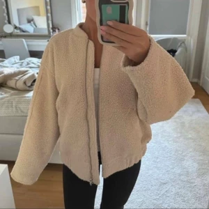 Beige teddyjacka från H&M - Mysig beige teddyjacka från H&M med dragkedja framtill och två fickor. Jackan har en avslappnad passform och är tillverkad i mjukt fleece-liknande material. Storlek S men skulle säga S/M