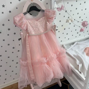 Rosa glittrig prinsessklänning med puffärm - Superfin rosa prinsessklänning med glittrig överdel, puffiga korta ärmar och pärldetaljer i midjan. Kjolen är i flera lager tyll med volanger och ger en riktigt sagolik känsla. Perfekt för dig som vill sticka ut och känna dig extra speciell.