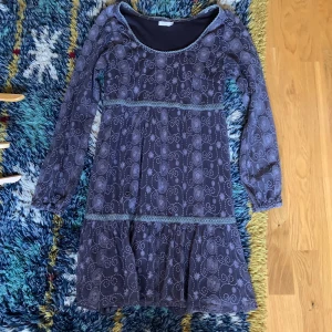 Lila mönstrad klänning med volang - Supersöt lila klänning med lång ärm och volang nertill. Klänningen har ett unikt mönster med snirkliga detaljer och markerad midja. Perfekt för dig som gillar boho-vibbar och vill ha något bekvämt men ändå snyggt.