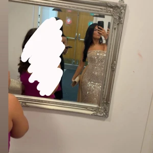 Festklänning  - Säljer en jättefin festklänning med glittriga paljetter och snörning i ryggen. Klänningen är axelbandslös med en figurnära passform upptill och ett svepande tylltyg nedtill. Perfekt för bal eller fest. Storlek Xs men passar även S. Endast använd en kväll. 