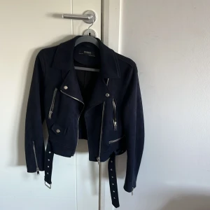 Mörkblå mocka bikerjacka Zara - Säljer en mörkblå bikerjacka från Zara med coola silverfärgade dragkedjor och bälte i midjan. Jackan är i mocka och har en croppad passform med långa ärmar och klassisk krage. Perfekt för dig som vill ha en edgy look.