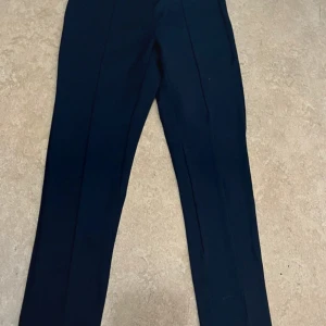 Mörkblå kostymbyxor Zara Kids 140 - Mörkblå kostymbyxor från Zara Kids i storlek 140. Byxorna har klassisk rak passform med pressveck framtill och resår i midjan för extra komfort. Perfekta för en stilren look och lätta att matcha med skjorta eller tröja.