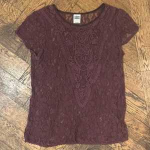 Vinröd spetstopp från Vero Moda - Supersnygg vinröd topp från Vero Moda i genombruten spets med korta ärmar och rund hals. Blusen har ett detaljerat broderat mönster framtill och är perfekt för dig som gillar spets och vill sticka ut lite extra. Det står S men skulle snarare säga att det är M