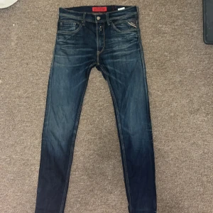 Replay Jondrill jeans blå, stl 31/32 - Snygga Replay Jondrill jeans i mörkblå tvätt med slitningar och coola kontrastsömmar. Klassisk femficksmodell med broderade bakfickor och röda detaljer på insidan. Slim fit. 