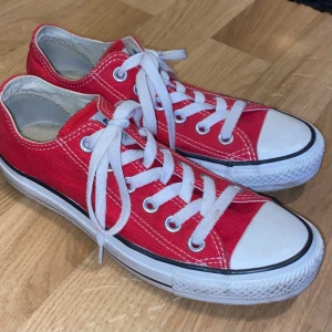 Röda Converse All Star sneakers - Klassiska röda Converse All Star sneakers med vit tå och vita snören. Lågt skaft, rund tå och platt sula. Ovandel i canvas med vita kontrastsömmar och svart rand på sulan. Perfekta för en avslappnad och cool stil.