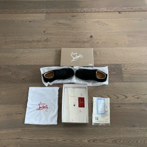 Svarta Christian Louboutin sneakers med spikar - Säljer ett par svarta sneakers från Christian Louboutin med coola svarta spikar på tån och klassisk röd sula. Skorna har snörning och är tillverkade i mocka med skinnfoder. Kommer med originalkartong, dustbag och tillbehör. Perfekt för dig som gillar edgy designerstil. Pris kan diskuteras vid snabbaffär