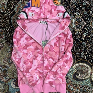 Bape hoodie - Säljer en helt ny och oanvänd Bape-hoodie i snygg rosa färg. Storlek M, men den passar dig som vanligtvis har storlek S. Som dessutom är både för killar och tjejer. Hoodien är i perfekt skick. Perfekt för dig som vill sticka ut med en unik och eftertraktad streetwear-look.  Pris: 699kr Skicka ett meddelande vid intresse! Kan mötas upp eller frakta.