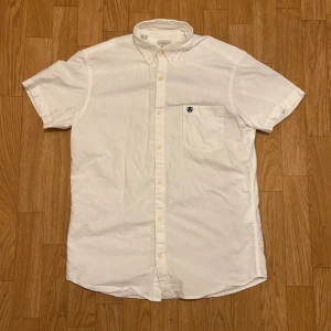 Vit kortärmad skjorta Selected Homme - Vit kortärmad skjorta från Selected Homme med klassisk button-down krage och bröstficka med broderad logga. Skjortan har en rak passform och är tillverkad i mjuk bomull, perfekt för varma dagar. Stängs med vita knappar framtill.