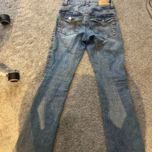 Blå bootcut jeans med fickdetaljer - Snygga ljusblå jeans med bootcut-modell och klassiska fem fickor. Jeansen har dekorativa sömmar och knappar på bakfickorna samt bälteshällor. Perfekta för dig som gillar en avslappnad men trendig look.