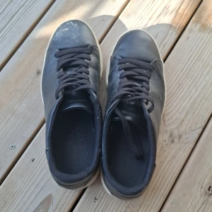 Svarta sneakers Selected Homme strl 43 - Stilrena svarta sneakers från Selected Homme i skinn med vita, platta sulor. Klassisk design med rund tå och svarta snören. Perfekta för dig som gillar minimalistisk look och vill ha ett par schyssta skor till vardags. Snygga och enkla att matcha med det mesta.