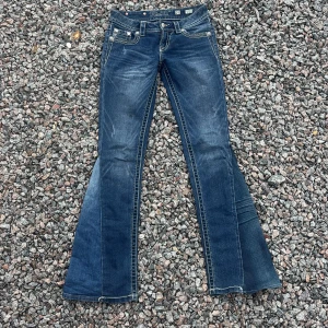 Miss Me blå bootcut jeans med brodyr - Snygga blå jeans från Miss Me med bootcut passform och coola broderade detaljer på bakfickorna. Jeansen har kontrastsömmar, dekorativa knappar och klassisk femficksdesign. Perfekta för dig som gillar statement-jeans med extra detaljer. Sytt ut dem så de nu är utsvängda. 