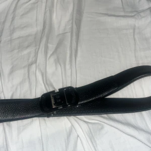 Svart burberry skärp  - Snyggt svart bälte i präglat skinn med ett stilrent metallspänne i svart med en stor B på. Bältet har en klassisk design och passar perfekt till jeans eller kostymbyxor. Ger en clean och modern look till outfiten.
