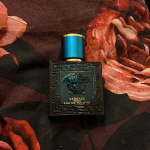 Versace Eros Eau de Toilette 30ml - Versace Eros Eau de Toilette i en snygg, turkosblå glasflaska med guldiga detaljer och Medusa-huvudet på framsidan. Flaskan rymmer 30 ml och har en lyxig, maskulin design med geometriskt mönster.