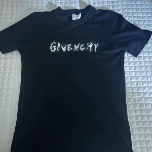 Svart Givenchy t-shirt med tryck - Svart t-shirt från Givenchy i bomull med vit logotyp framtill och stort grafiskt tryck på ryggen. Klassisk passform och rund hals. Perfekt för dig som vill sticka ut med en lyxig streetstyle-look. Storlek S men passar även M, knappast använd 