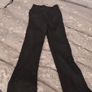 Svarta bootcut byxor med rynkdetalj - Säljer ett par svarta bootcut byxor i stretchigt material med snygg rynkdetalj framtill i midjan. Byxorna är högmidjade och tillverkade i 92% polyester och 8% elastan, vilket gör dem både bekväma och följsamma. Perfekta för dig som gillar en trendig och stilren look.