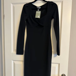Svart långärmad klänning H&M - Snygg svart långärmad klänning från H&M med figurnära passform och djupare urringning. Klänningen har en stilren design och är perfekt för dig som gillar en enkel men elegant look.