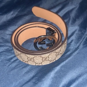 Gucci GG  - Snyggt Gucci GG Supreme bälte i beige och brunt med klassiskt monogrammönster och GG-spänne i silver. Bältet är gjort i skinn och canvas, perfekt för att lyfta vilken outfit som helst. Kommer med originalbox och dustbag.