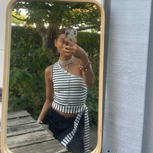 Randig one shoulder topp med knyt - Säljer en svartvit randig one shoulder topp med knyt i midjan. Toppen är croppad och har breda ränder som ger en fräsch och trendig look. Perfekt för dig som vill sticka ut med en cool och modern stil.