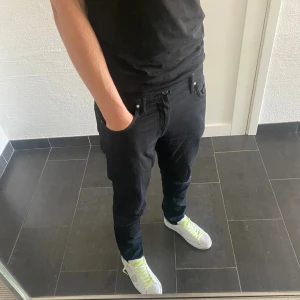 Svarta jeans från Tiger of Sweden - Säljer ett par svarta jeans från Tiger of Sweden med klassisk femficksdesign och snygg passform. Jeansen har en stilren look, raka ben och är tillverkade i bomull med en skön stretch. Perfekta för dig som gillar en clean och modern stil.