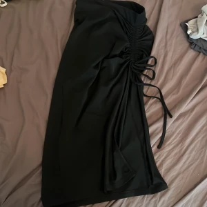 Svart långkjol med snörning - Snygg svart långkjol med slits snörningsdetalj på sidan som ger en draperad effekt. Kjolen har en stilren look. Materialet känns mjukt och följsamt, vilket gör den bekväm att bära hela dagen. 