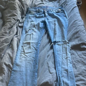 Ljusblå slitna jeans med hål - Säljer ett par ljusblå jeans med stora slitningar och hål på båda benen. Jeansen har klassisk femficksdesign och raka ben. Perfekta för dig som gillar en avslappnad och edgy stil. Materialet är denim och de har en cool, sliten look. Är 168 och dem är en decimeter för långa för mig PRIS KAN DISKUTERAS Waist 28 lenght 34