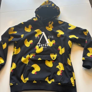 Skidjacka med ankor  - Svart hoodie från Slade  med stora gula ankmotiv över hela tröjan. huva och magficka med knappar. Mjuk insida och ribbade muddar. Den är i gott skick! Jag säljer även en matchande hjälm till så kolla min profil om ni är intresserade 🦆det står storlek 170 men jag har S/M annars och den passar hur bra som helst. Väldigt sparsamt använd 