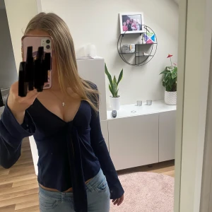 Mörkblå omlottopp från Gina Tricot - Säljer en mörkblå omlottopp från Gina Tricot i storlek XS. Toppen har djup v-ringning, långa ärmar och knyt framtill. Tunt och lätt material som ger en snygg och feminin look. Perfekt att styla med jeans eller kjol. Tröjans skick är bra det är inga hål eller slitningar på den.