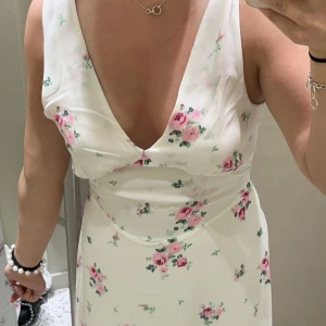 Vit blommig långklänning  - Supersöt långklänning från Bik Bok i vit med rosa blommor. Klänningen har djup v-ringning och har band som sitter på axelbanden. Använd fåtal gånger, i fint skick!💞
