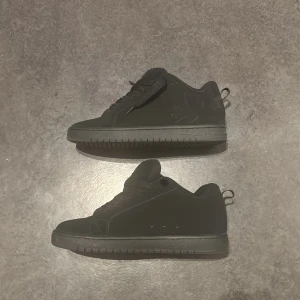 Svarta DC sneakers med snörning - Helmatta svarta sneakers från DC Shoes med klassisk låg profil och rund tå. Skorna har snörning, diskret DC-logga på sidan och dragflik bak. Ovandelen är i syntetmaterial och sulan är platt och greppvänlig. Perfekta för en clean streetstil.