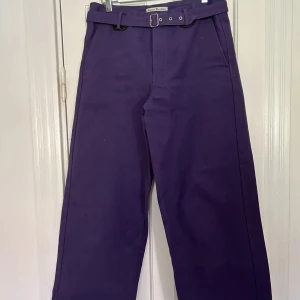 Lila byxor med bälte från Acne Studios - Snygga lila byxor från Acne Studios med tillhörande bälte och raka ben. Byxorna har fickor fram och bak, och är tillverkade i ett kraftigare bomullstyg. 