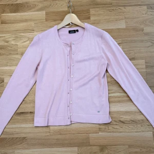 Säljer Ljusrosa kofta från KappAhl! - Tröjan är helt ny och är endast använd ett fåtal gånger.  Storlek på tröjan: S. Pris: 200kr  Supersöt ljusrosa kofta från KappAhl med rund halsringning och långa ärmar. Koftan har knappar hela vägen framtill och är gjord i mjuk bomull, perfekt att slänga över en topp. Enkel och stilren design som passar till allt.