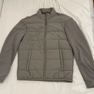 Säljer Höst/Vår Jacka! - Storlek: S  Jackan har inga fläckar eller skador och är som helt ny. Endast använd 3 gånger. Säljer en stilren grå pufferjacka med hel dragkedja framtill och två fickor. Jackan har quiltad framsida och släta ärmar, perfekt för kyligare dagar. Enkel design med hög krage och elastisk nederkant. 