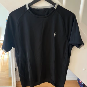 Svart t-shirt från Ralph Lauren - Svart träningst-shirt från Ralph Lauren med klassisk vit logga på bröstet. T-shirten har rund halsringning och korta ärmar. Materialet är mjukt och stretchigt.