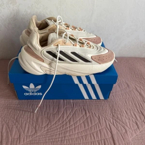 Adidas ozelia sneakers i beige och rosa - Adidas ozelia sneakers med chunky sula i beige och ljusrosa med svarta detaljer på sidorna. Ovandelen är i syntet och mocka, med vita snören och coola vågformade linjer.