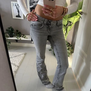 Grå bootcut jeans från Gina  - Säljer ett par grå jeans från Perfect Jeans i storlek 36. Modellen har bootcut-ben, låg midja och klassiska fem fickor med snygga detaljer på bakfickorna. Jeansen är i mjukt denim-material och har en cool, tvättad look.